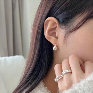 Close-up of minimalist silver teardrop earrings and layered knot ring on a model