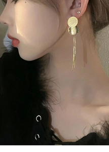 Detail of long gold tassel earrings with textured circular elements on a model