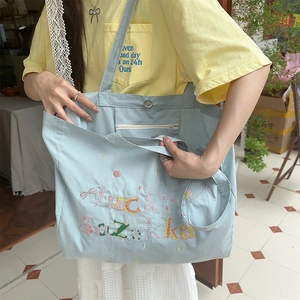 Détail d'un sac cabas en toile bleu clair avec broderie lucky et fermeture à pression