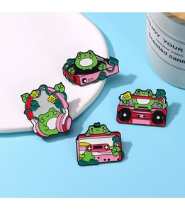 Detailed view of four cartoon frog enamel pins with musical themes on a white ceramic plate