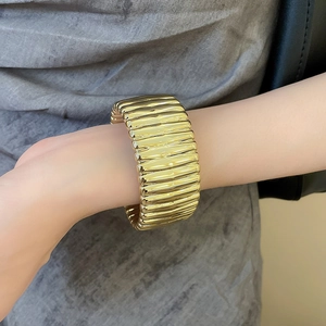 Detailed close-up of a wide gold ribbed metal cuff bracelet on a female wrist