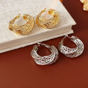 Detailed macro view of gold and silver hollow hoop earrings with Greek Meander patterns