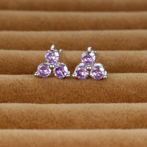 Macro detail of purple gemstone clover stud earrings set in silver metal on brown velvet