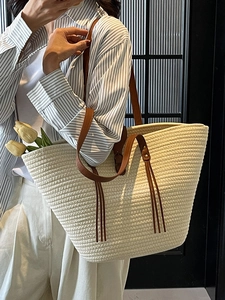 Large beige woven tote bag with brown straps and fringe, styled on a model for beach fashion