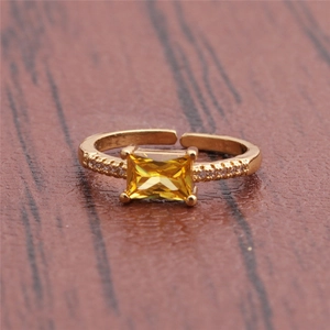 Macro detail of gold plated ring featuring rectangular yellow gemstone and crystal accents