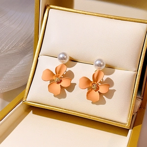 Close-up of orange-pink flower earrings with white pearls in a golden gift box