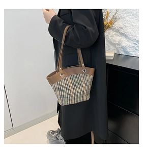 Detail of wool plaid bucket bag with brown leather trim and metal handle rings