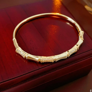 Detailed view of gold plated bamboo style bracelet with cubic zirconia on a wooden box