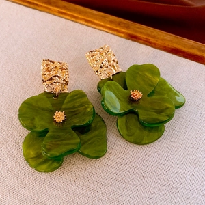 Detailed macro of dark green acrylic flower earrings with textured golden metal studs