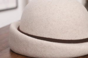 Detail of oatmeal wool beret showing thick felt texture and dark brown decorative band
