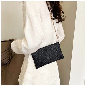 Detailansicht einer schwarzen Glitzer-Umschlagtasche mit goldener Kette an einem Modell
