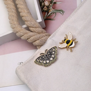 Détail de broches vintage émaillées abeille et papillon sur un sac en toile