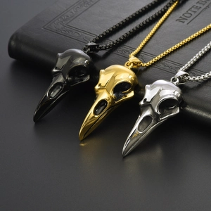 Gothic punk raven skull necklaces in black, gold, and silver finishes on a notebook