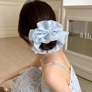 Gros plan d'un chouchou bleu clair en seersucker à bords volantés sur un chignon de mannequin