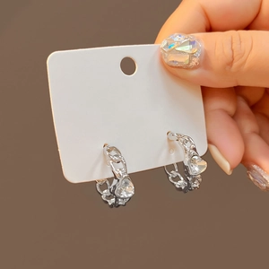 Detail of silver heart-shaped zircon earrings held by hand on a neutral background