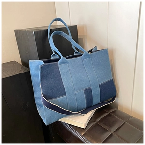 Detail of a geometric patchwork denim tote bag with blue and beige wide shoulder strap