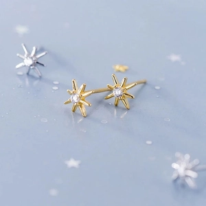 Macro detail of gold eight-point star stud earrings with sparkling round white zircon stones