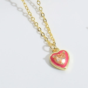 Macro shot of gold heart pendant with pink enamel and bright orange zircon center