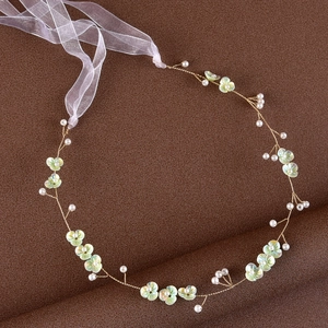 Close-up of bridal headband with light green flowers, gold wire, and pearls on brown base