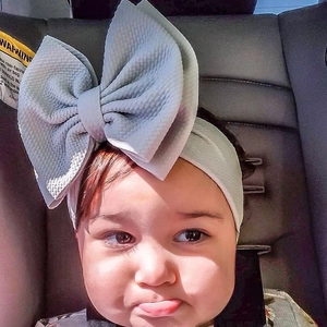 Close-up of a light grey ribbed fabric baby headband with a large bow worn by a toddler