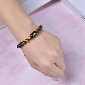 Bracelet fait main en œil de tigre avec perle initiale A porté sur fond de marbre rose