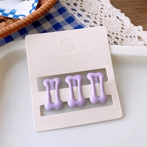 Detailed view of three cute purple bone-shaped hair clips on a white accessory display card
