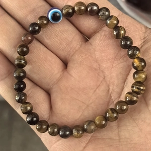Detail shot of tiger eye stone beads and a blue evil eye charm held in palm