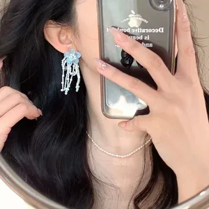 Macro view of light blue floral earrings with delicate white beaded tassels and pearls