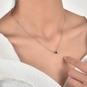 Close-up of a silver clavicle chain with a round black zircon pendant worn by a model