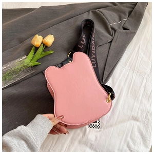 Detail of pink bear-shaped crossbody bag with black lettered strap on cozy bedding