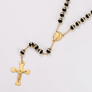 Detail view of gold rosary necklace with black beads, virgin mary medal and crucifix