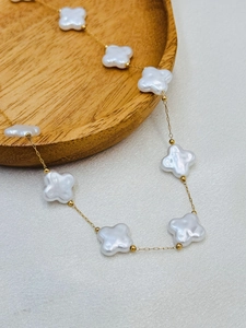 Detailed close-up of golden clover necklace with iridescent white shell charms