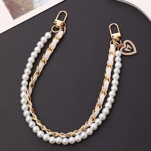 Detail of luxury pearl and chain strap with black heart charm and gold bow for phone bags