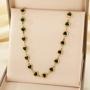 Close-up of a gold necklace with a green heart glass pendant on beige satin lining