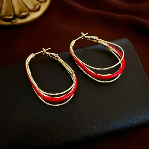 Macro detail of gold earrings with red enamel on a luxury black textured background