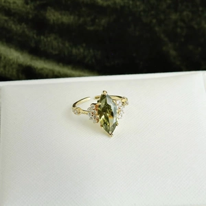 Macro view of gold-plated ring with olive green marquise zircon and side accents