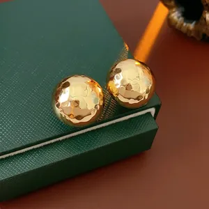 Golden domed earrings with hammered metal texture displayed on a green jewelry box