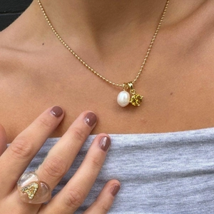 Close-up of a gold pearl necklace with a yellow gem and a transparent letter A ring