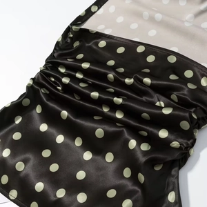 Detailansicht aus schwarzem Satin mit grünen Punkten und geraffter, gefalteter Textur
