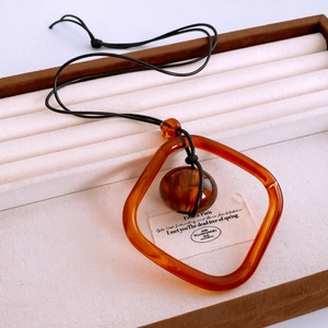 Gros plan du pendentif carré en résine orange sur cordon de cire noire en boîte à bijoux