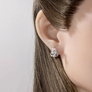 Delicate silver bow and snowflake stud earrings with pink and blue gemstones on ear