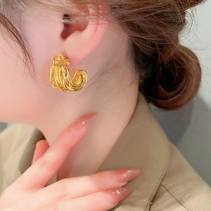 Close-up of golden multi-layered C-shaped earrings with twisted lines on a model