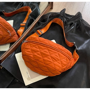 Detail of an orange quilted crossbody bag with adjustable strap and textured diamond pattern