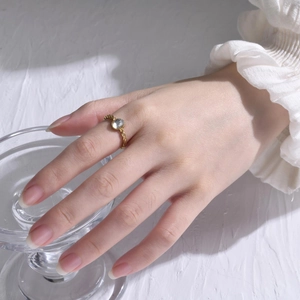 Elegant gold twisted steel ring with clear oval zircon worn on hand over glass