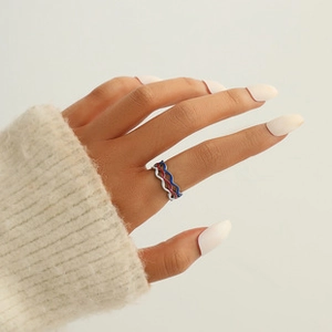 Close-up of three stacked wavy rings in gold silver and blue on a model hand