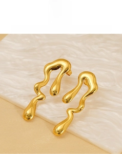 Macro shot of polished gold liquid metal geometric earrings on white marble surface