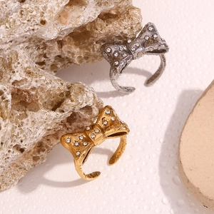Close-up of gold and silver bowknot rings with micro-inlaid crystals on stone