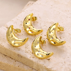 Macro shot of gold moon earrings set with colorful zircon on a textured stone surface