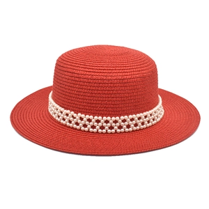 Detailed shot of red straw hat featuring a woven texture and three-row pearl mesh band