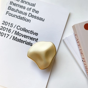 Makroansicht der mattgoldenen flüssig-geformten Handyhalterung auf Designmagazin